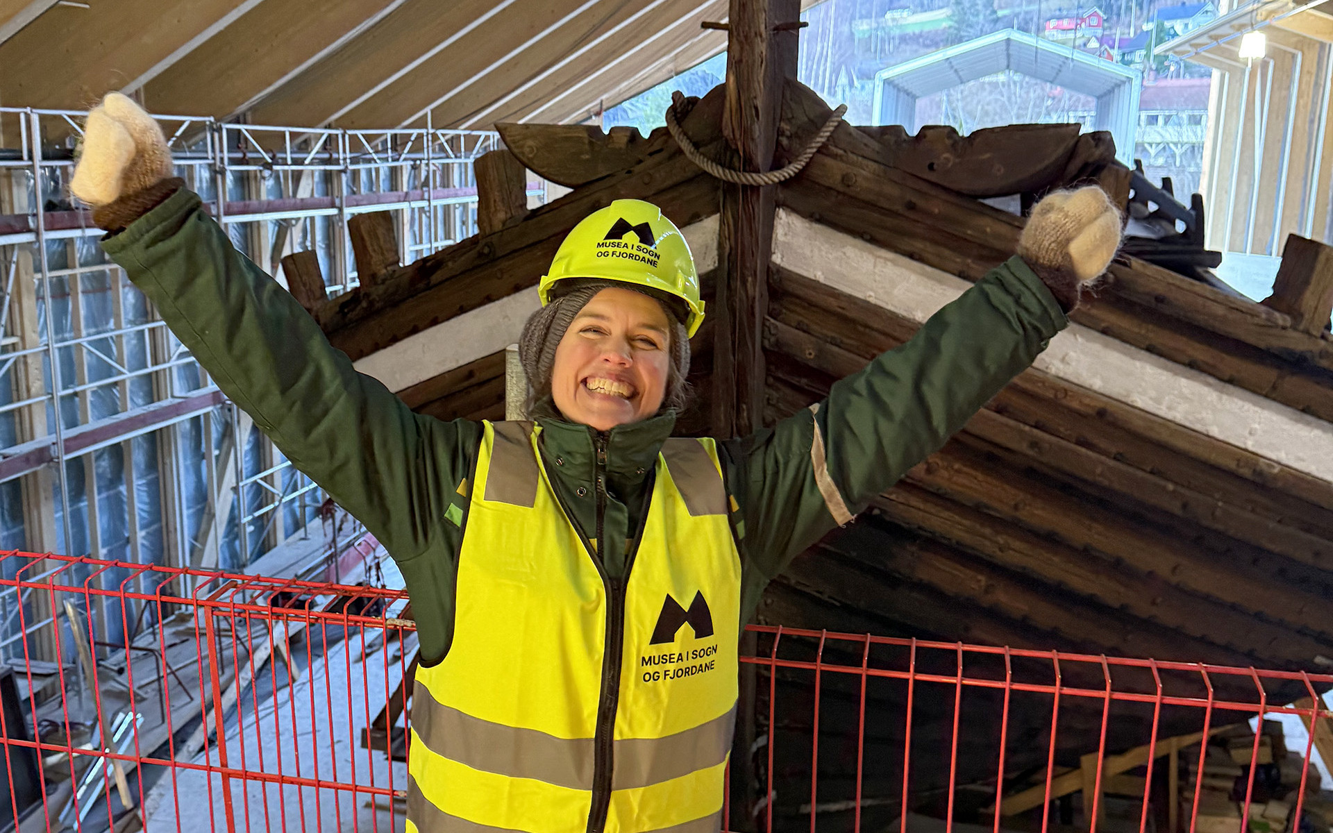 Dame med hjelm og arbeidsvest som strekk armane i veret