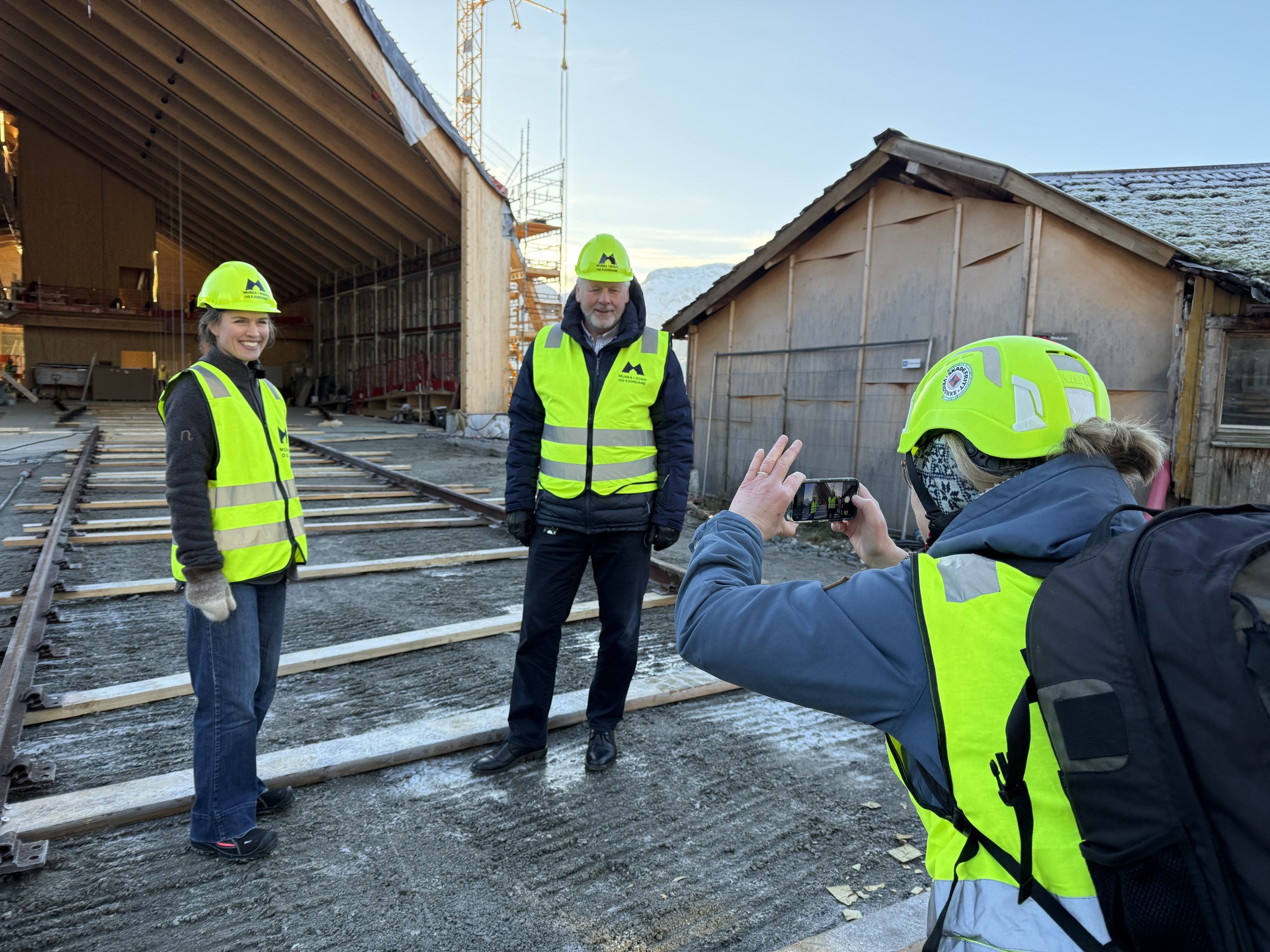 Journalist fotograferer to personar med gul hjelm og arbeidsvest.