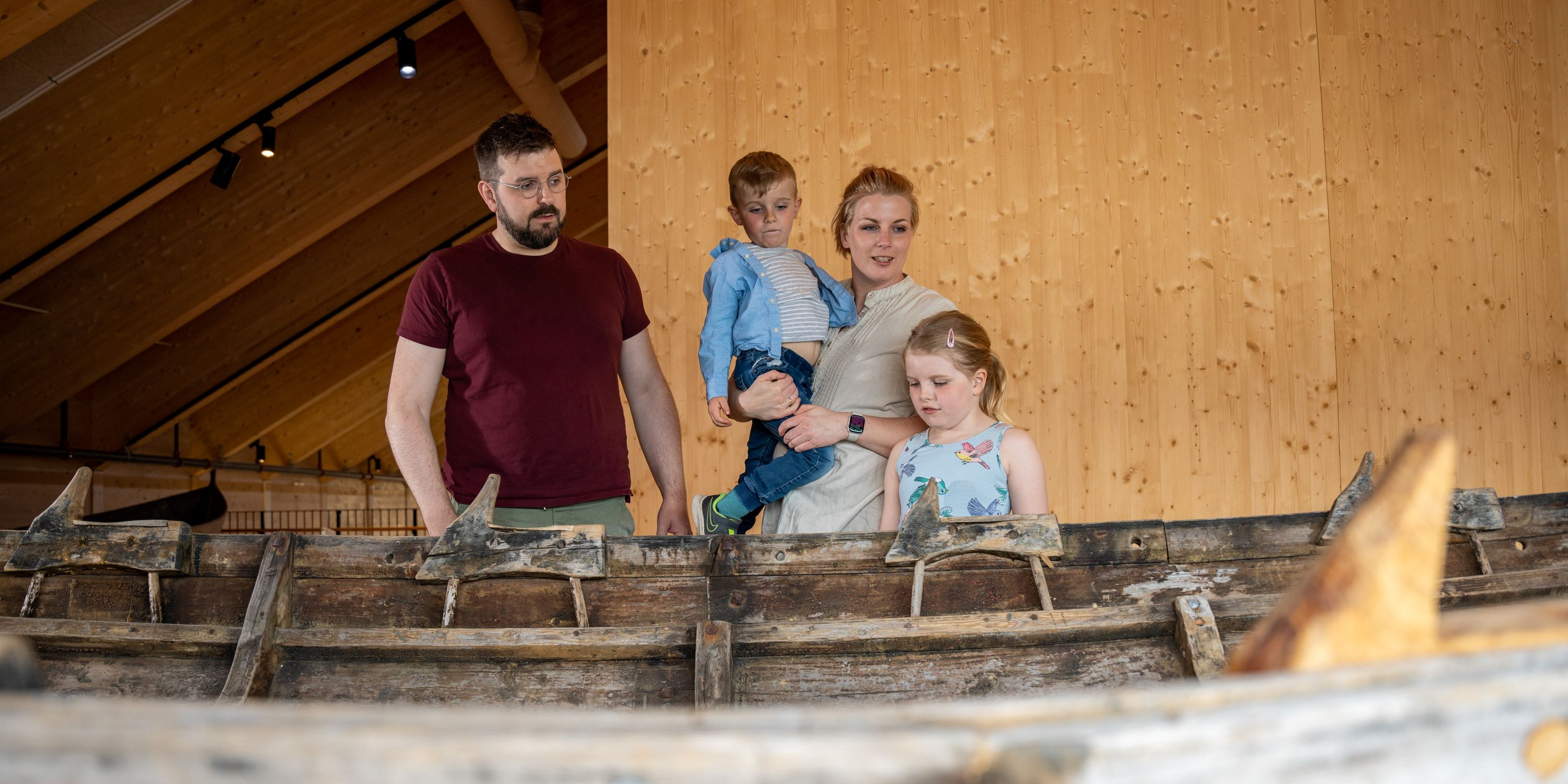 En familie på mor, far og to barn som ser på en båt laget av tre.