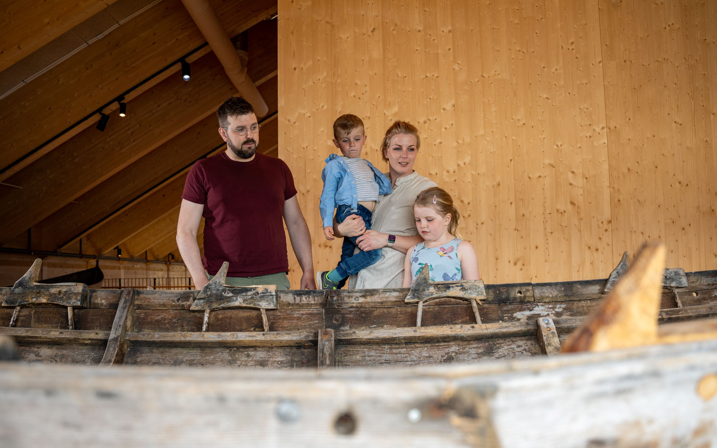 En familie på mor, far og to barn som ser på en båt laget av tre
