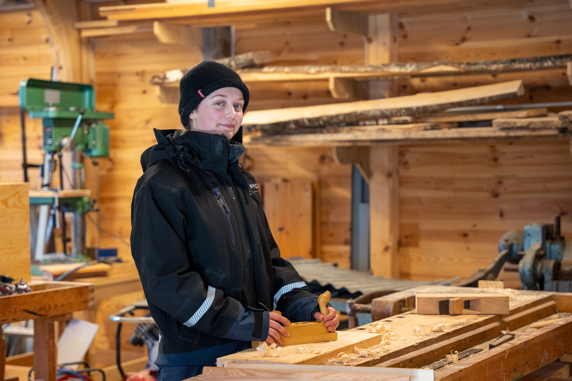 Ung kvinne med arbeidsklede ved høvlebenk, held handhøvel.