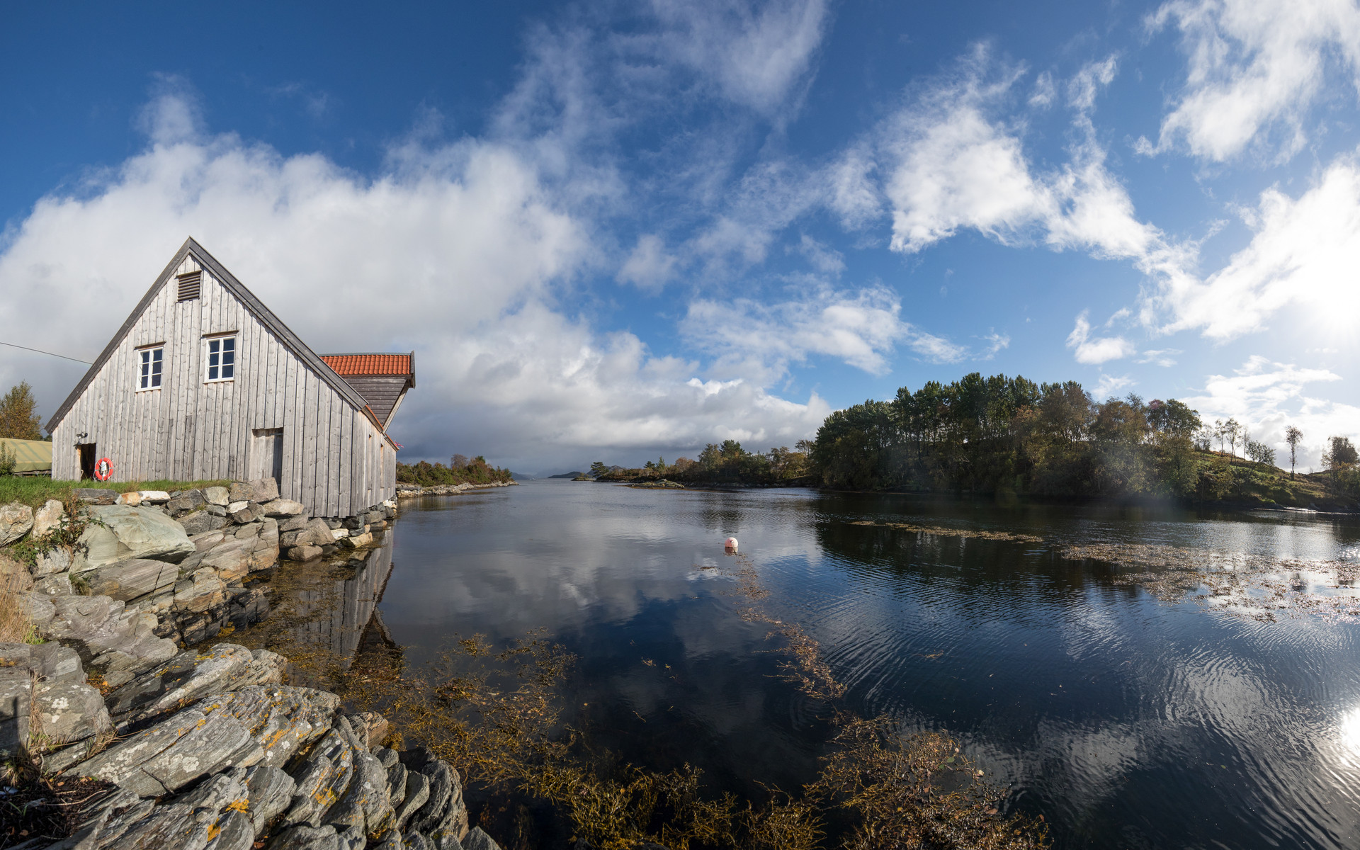 Oversiktsbilde over Bataldebua ved sjøen og Brendøya i bakgrunnen. Blå himmel og rolig sjø.