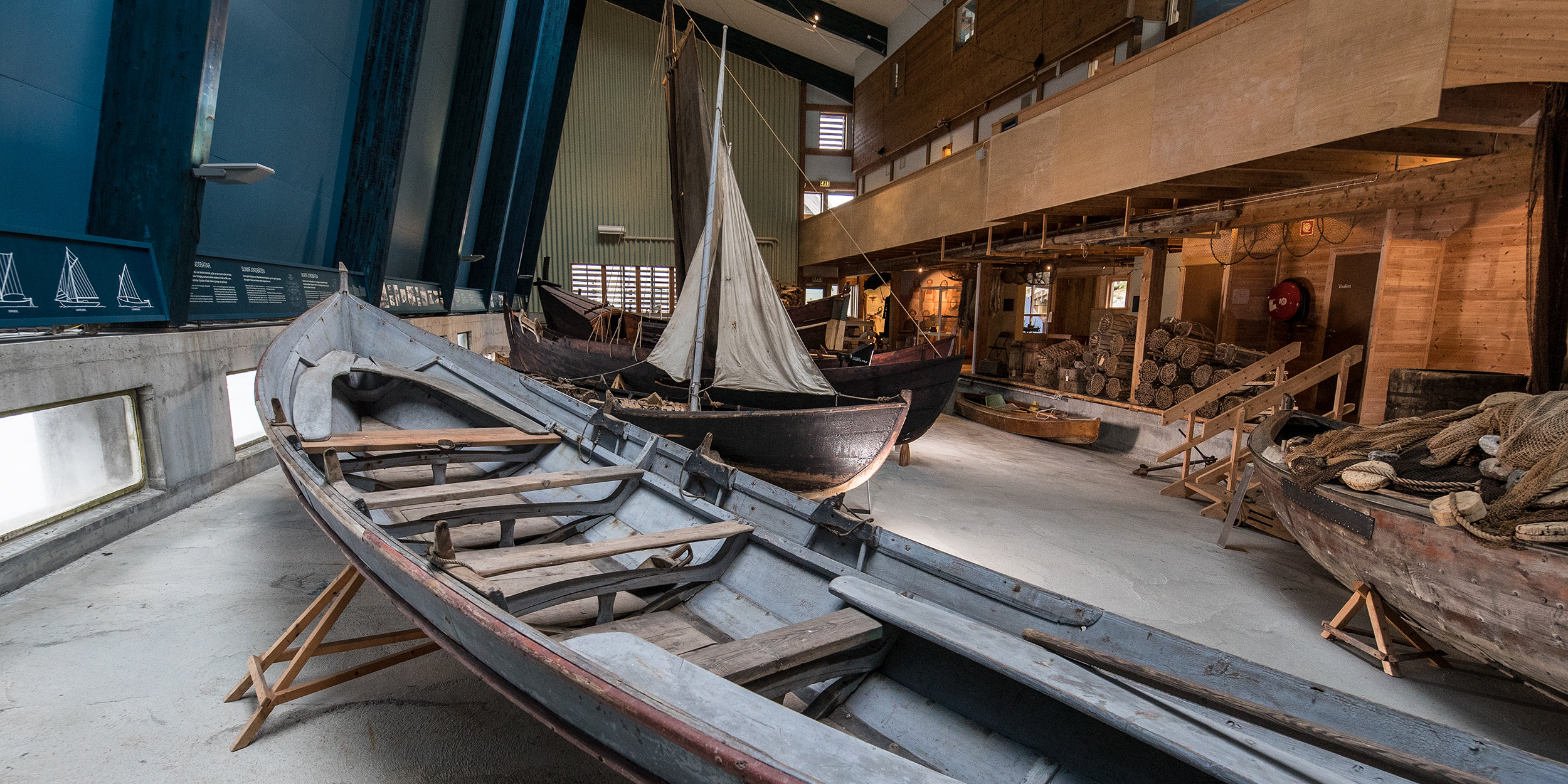 Oversiktsbilde over båthallen på Kystmuseet med fleire eldre trebåtar, teiner og garn.