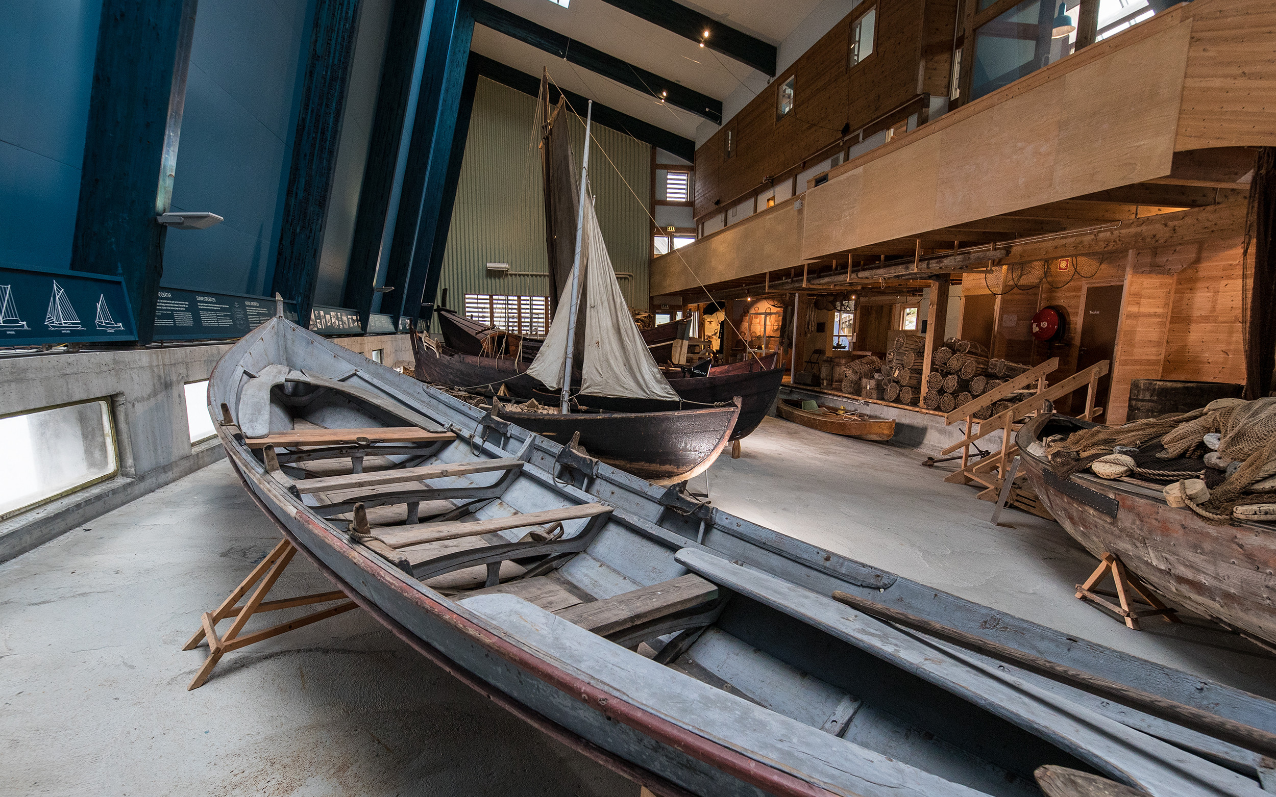 Oversiktsbilde over båthallen på Kystmuseet med fleire eldre trebåtar, teiner og garn.