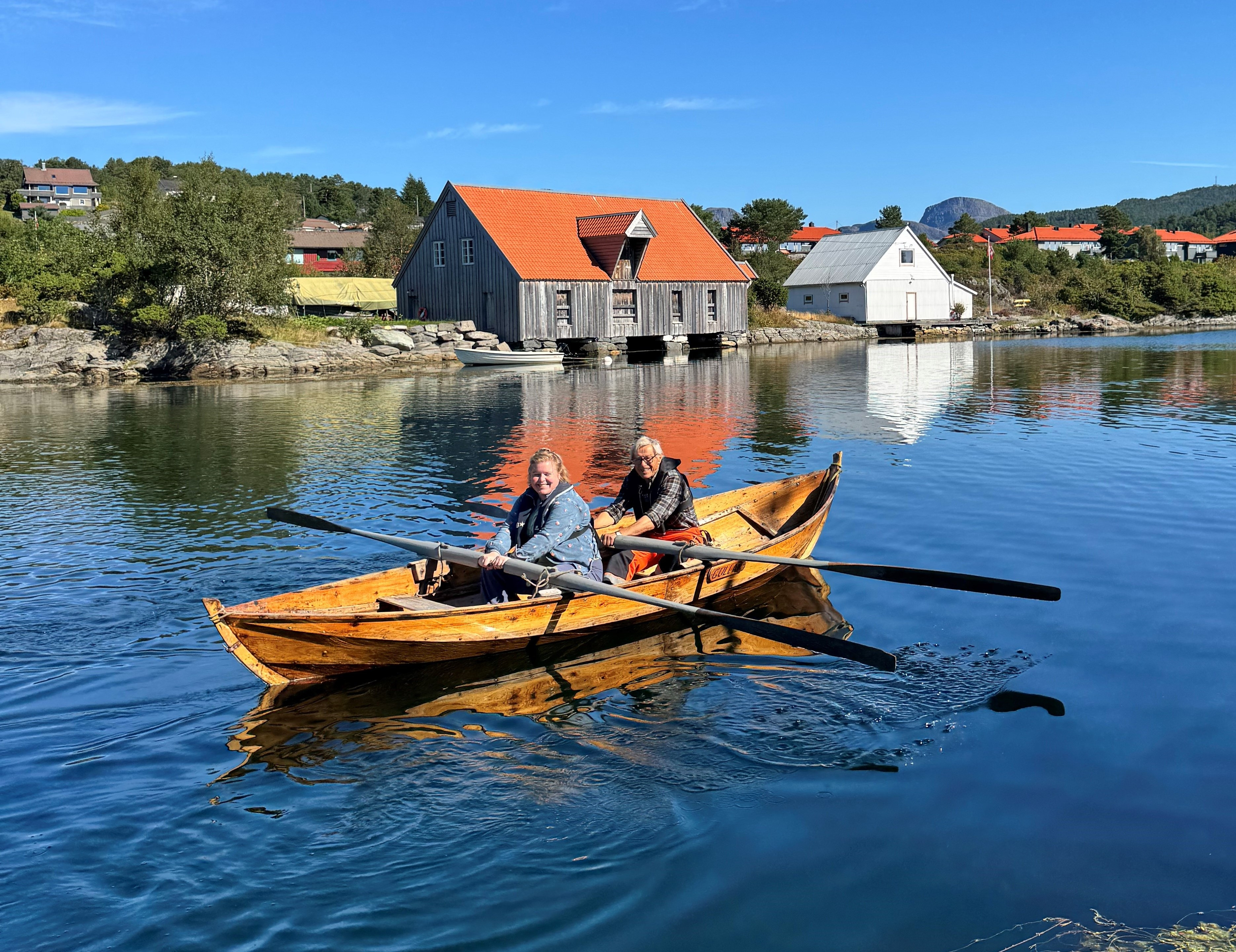 To personar ror ein gamal trebåt på fjorden.