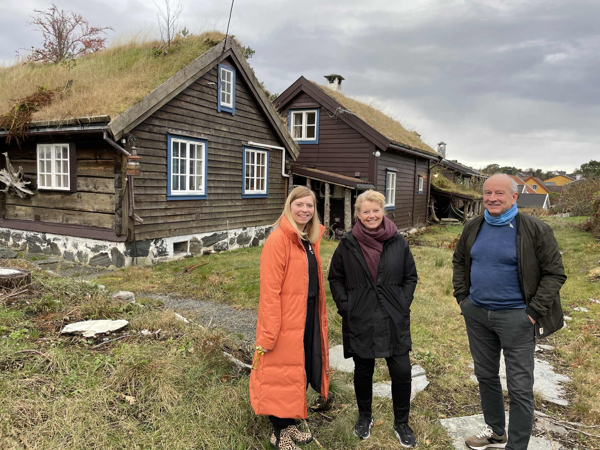 Tre personar smiler framfor eldre bygningar.