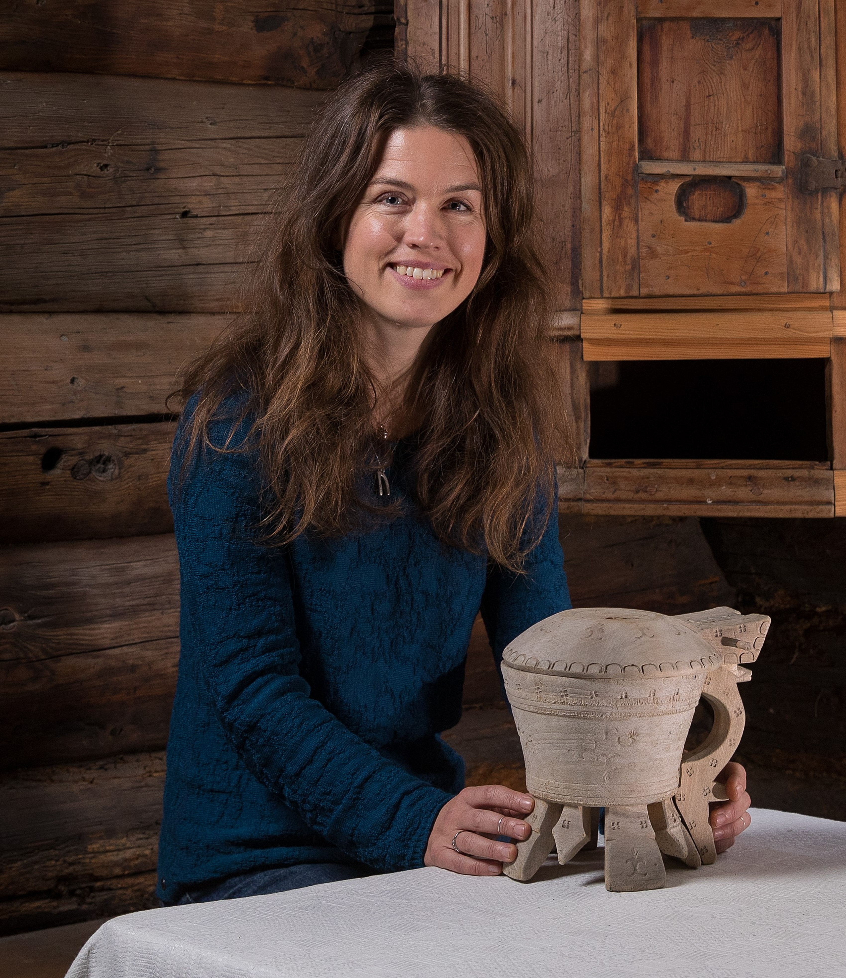 Portrett av Anne Kristin Moe i eit gamalt hus med ei smør-krukke framfor seg.