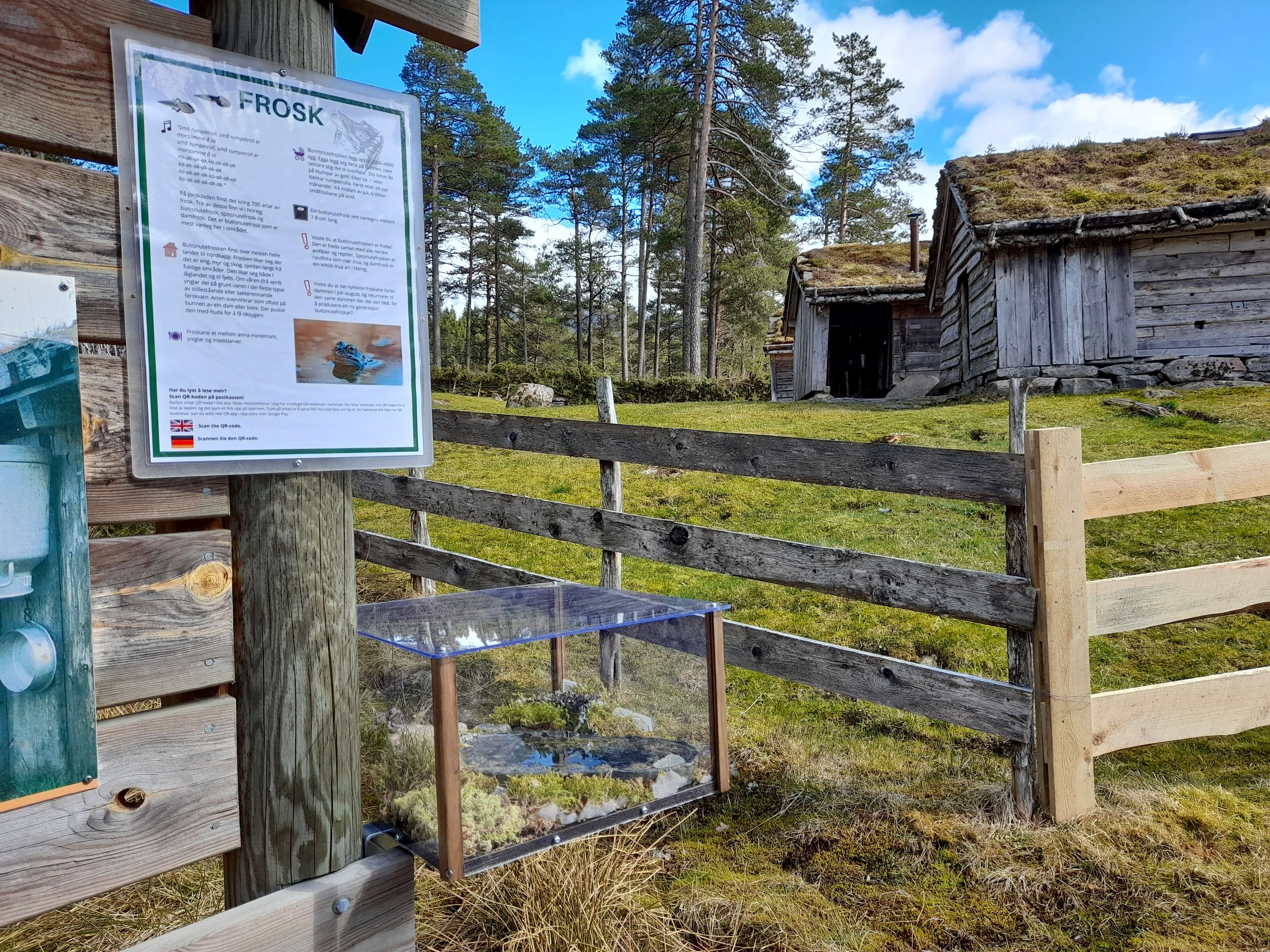 Monter og plakat montert ute i eit landskap. Gamle bygningar i bakgrunnen.