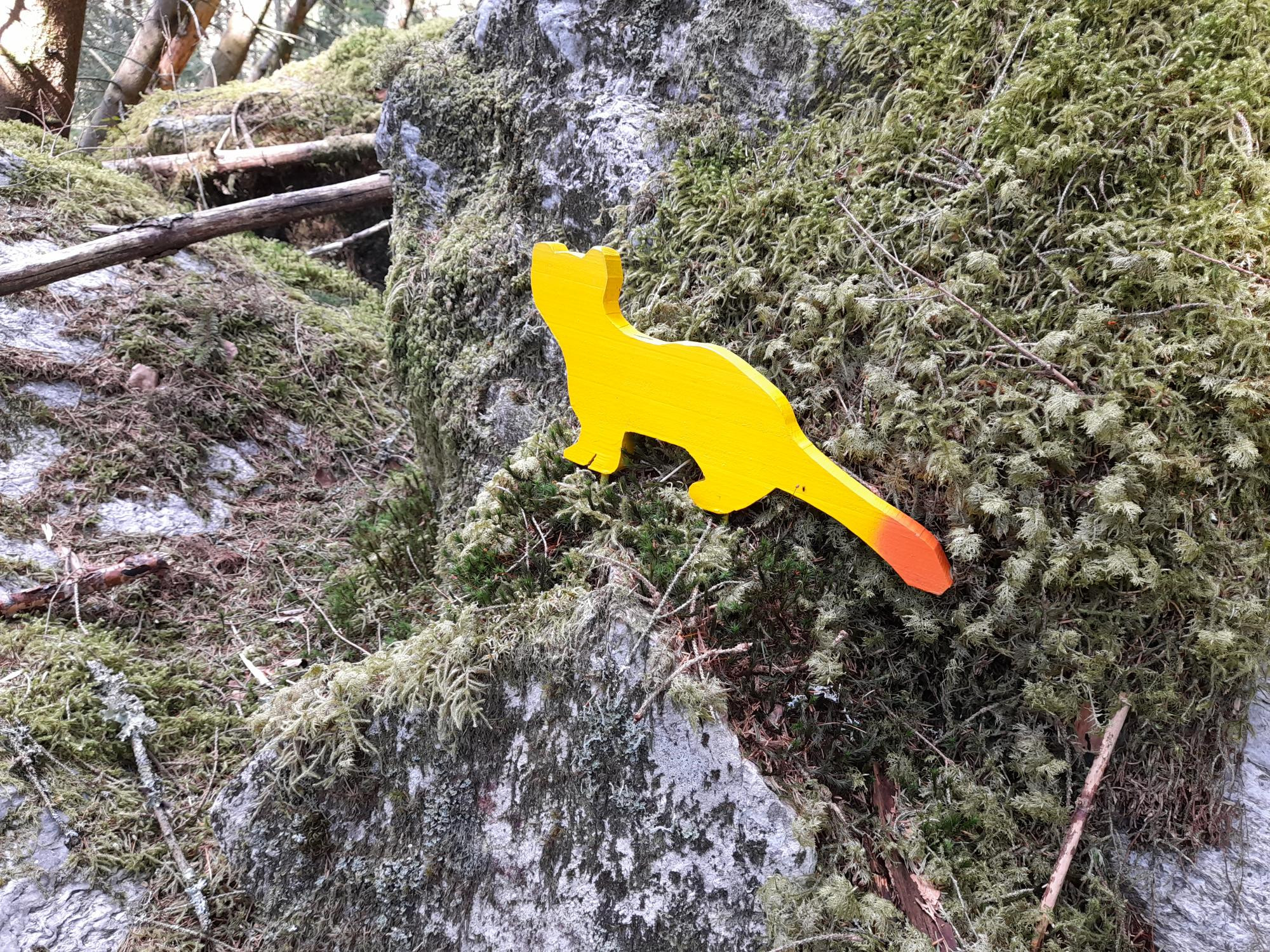 Dyrefigur i sterk gulfarge står ute i skogen.