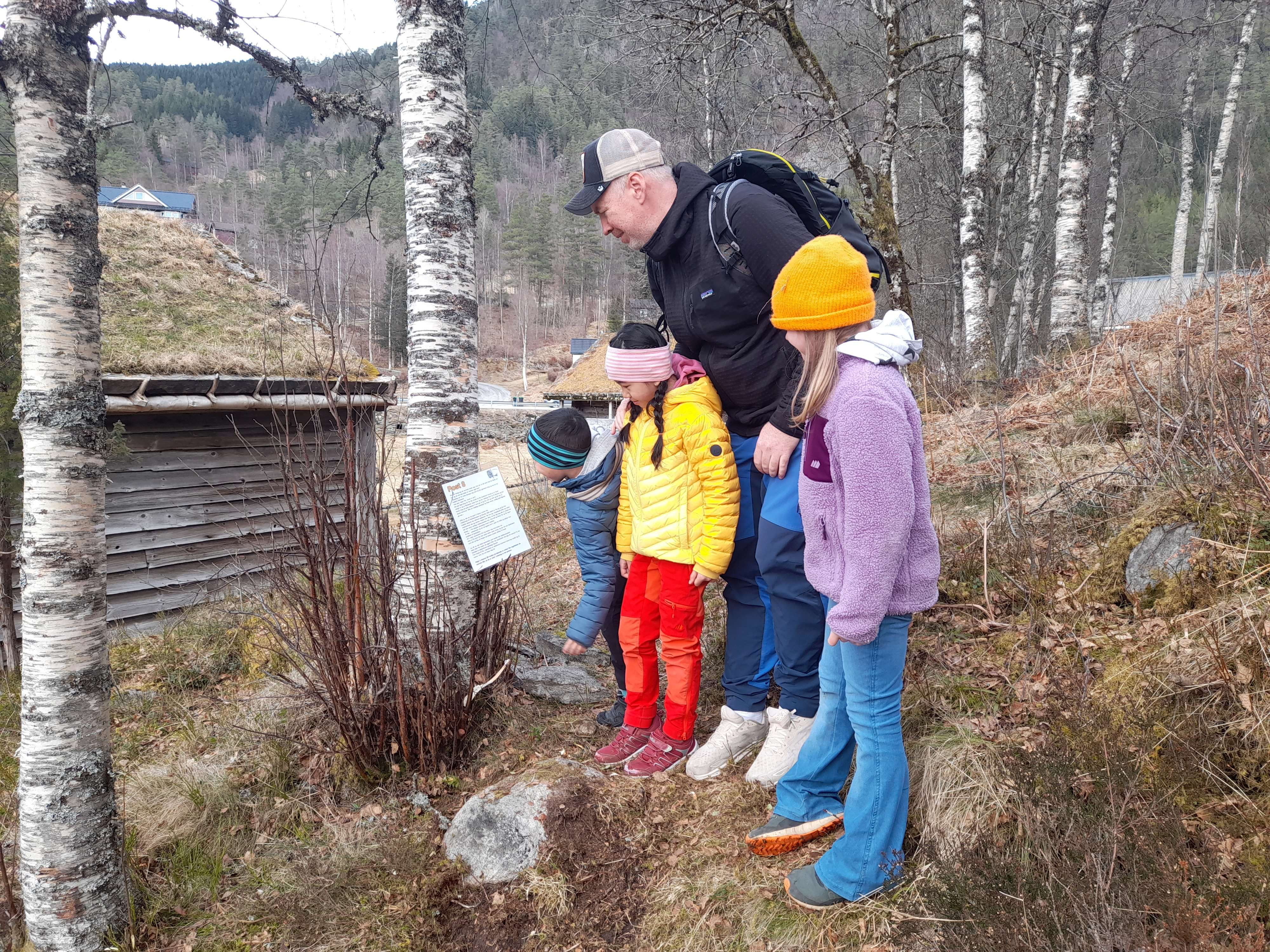 Tre born og ein mann les på eit skilt som heng på eit tre.