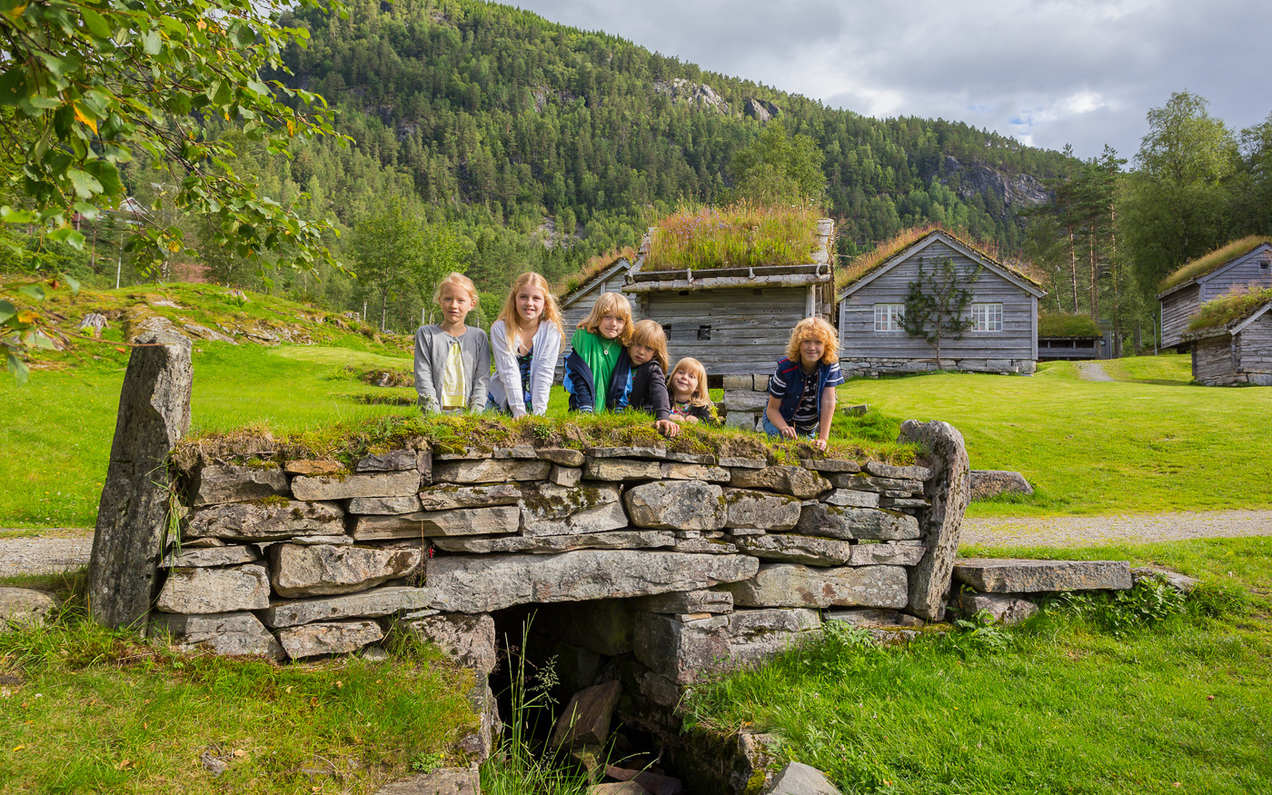 Barn står på ei steinbru i friluftsmuseet. Antikvariske hus i bakgrunnen.