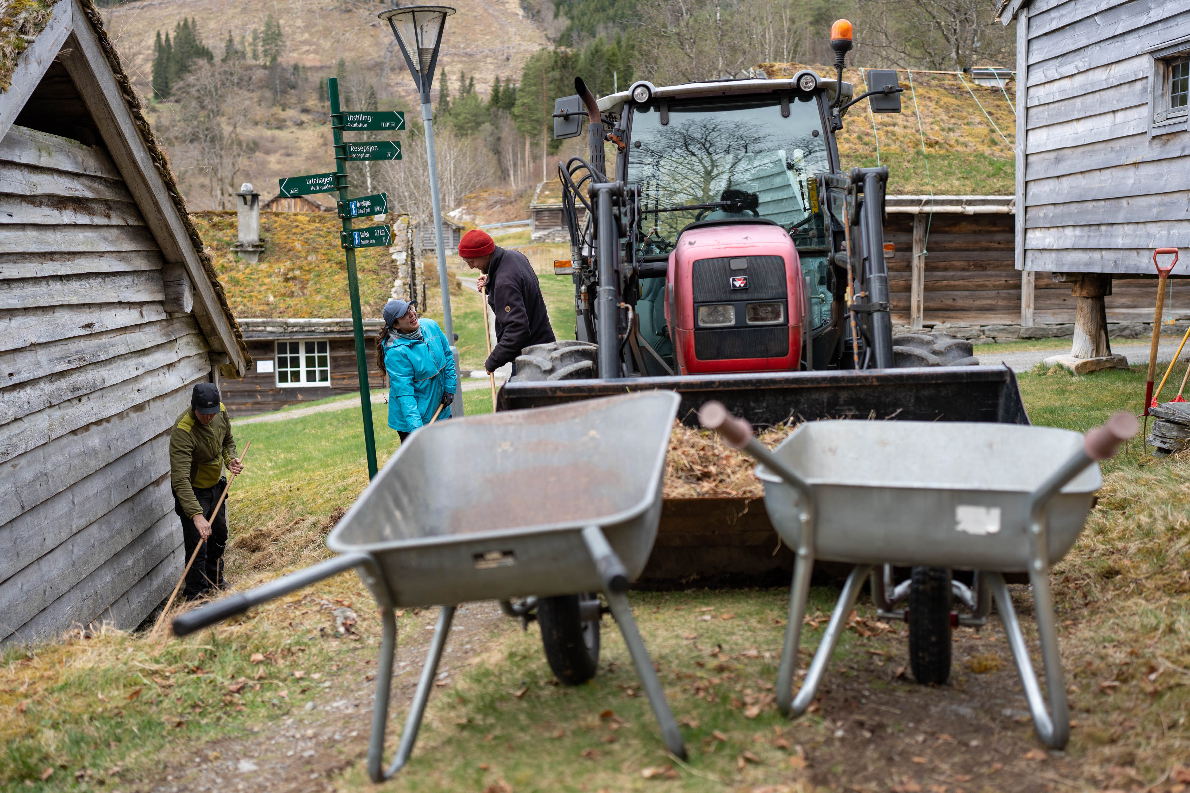 to trillebårer framme. Bak ein traktor og tre personar i arbeid.