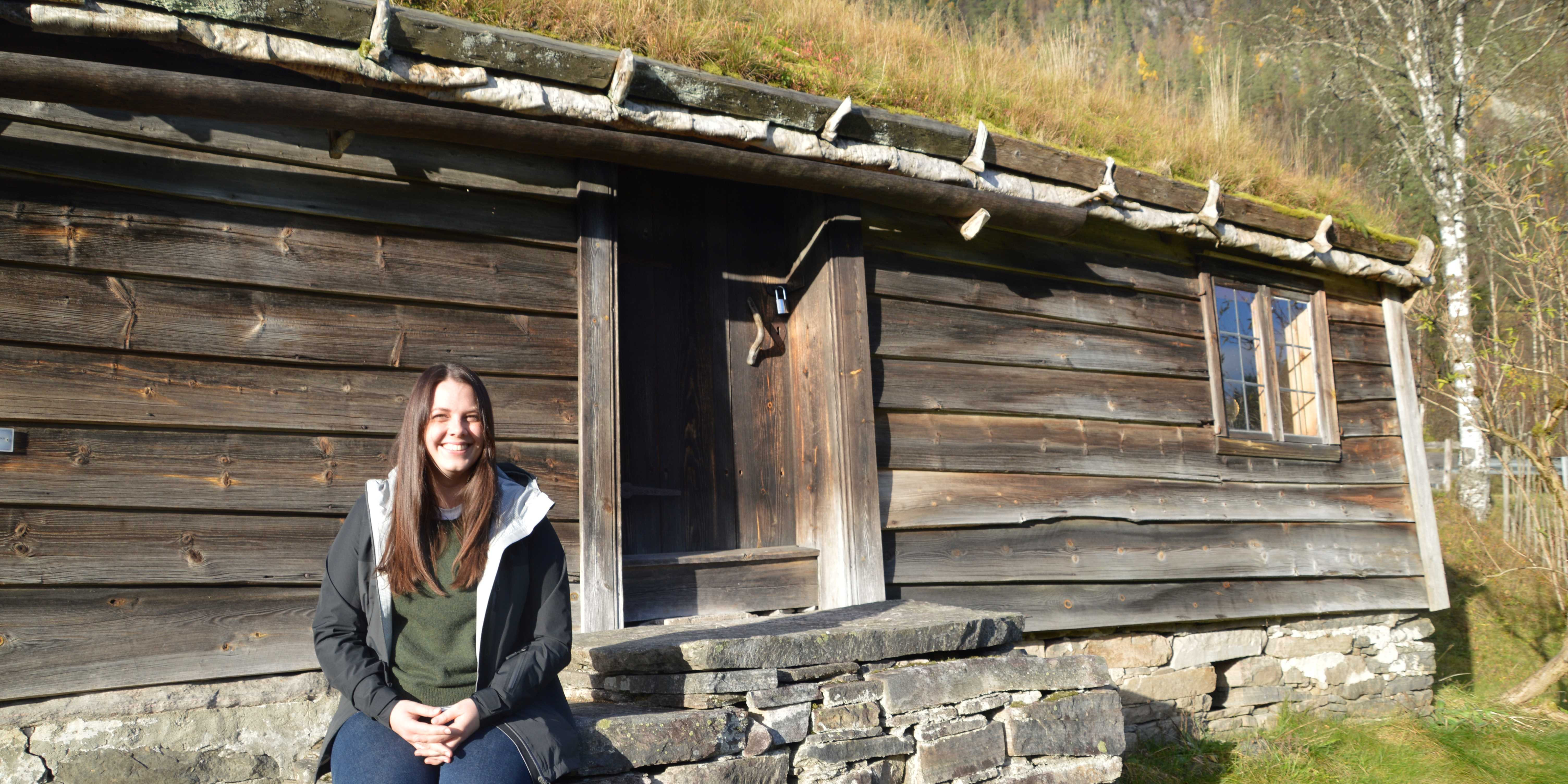 Konservatoren Kristine Ness sit foran huset på husmansplassen på Sunnfjord Museum.