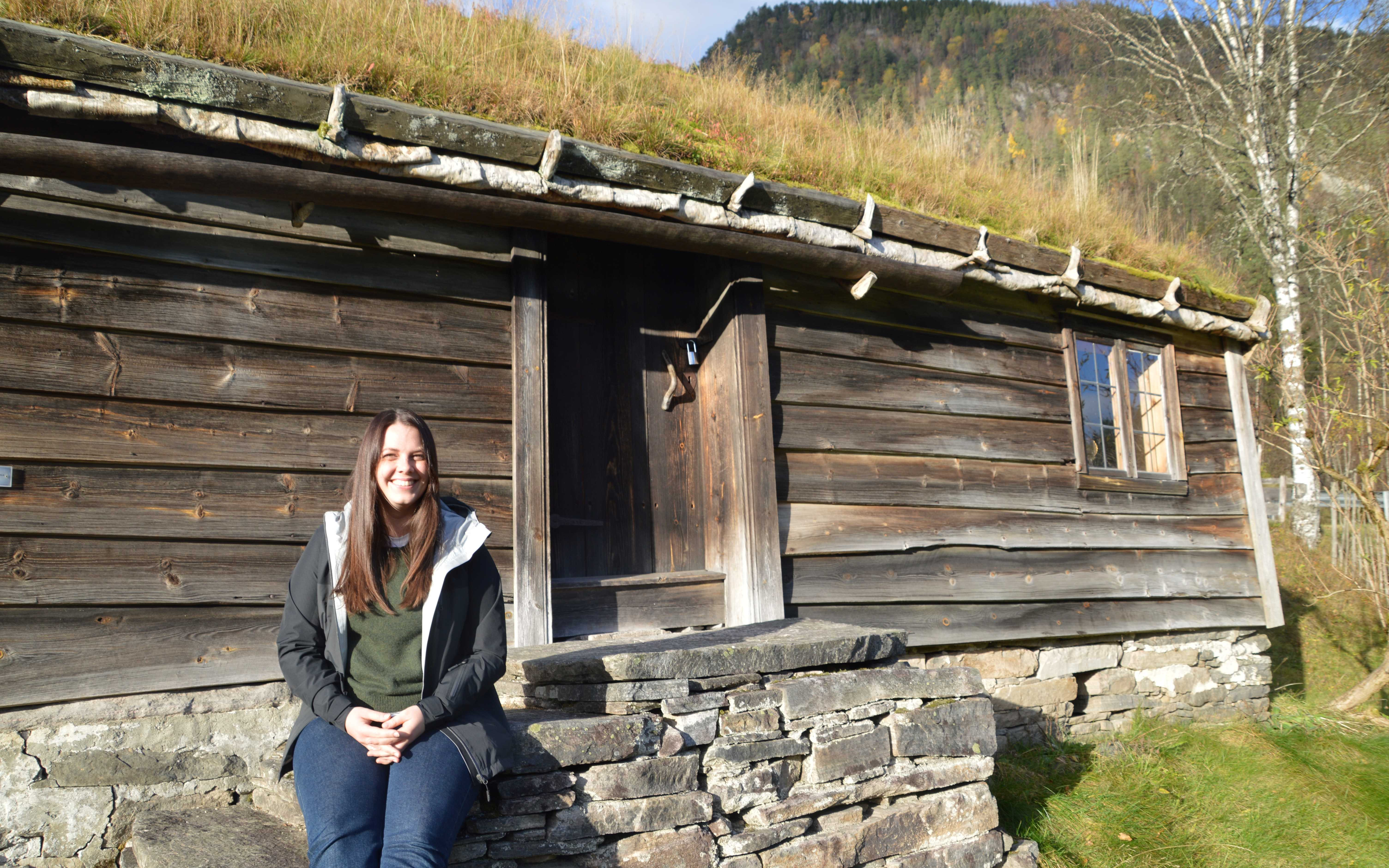 Konservatoren Kristine Ness sit foran huset på husmansplassen på Sunnfjord Museum.