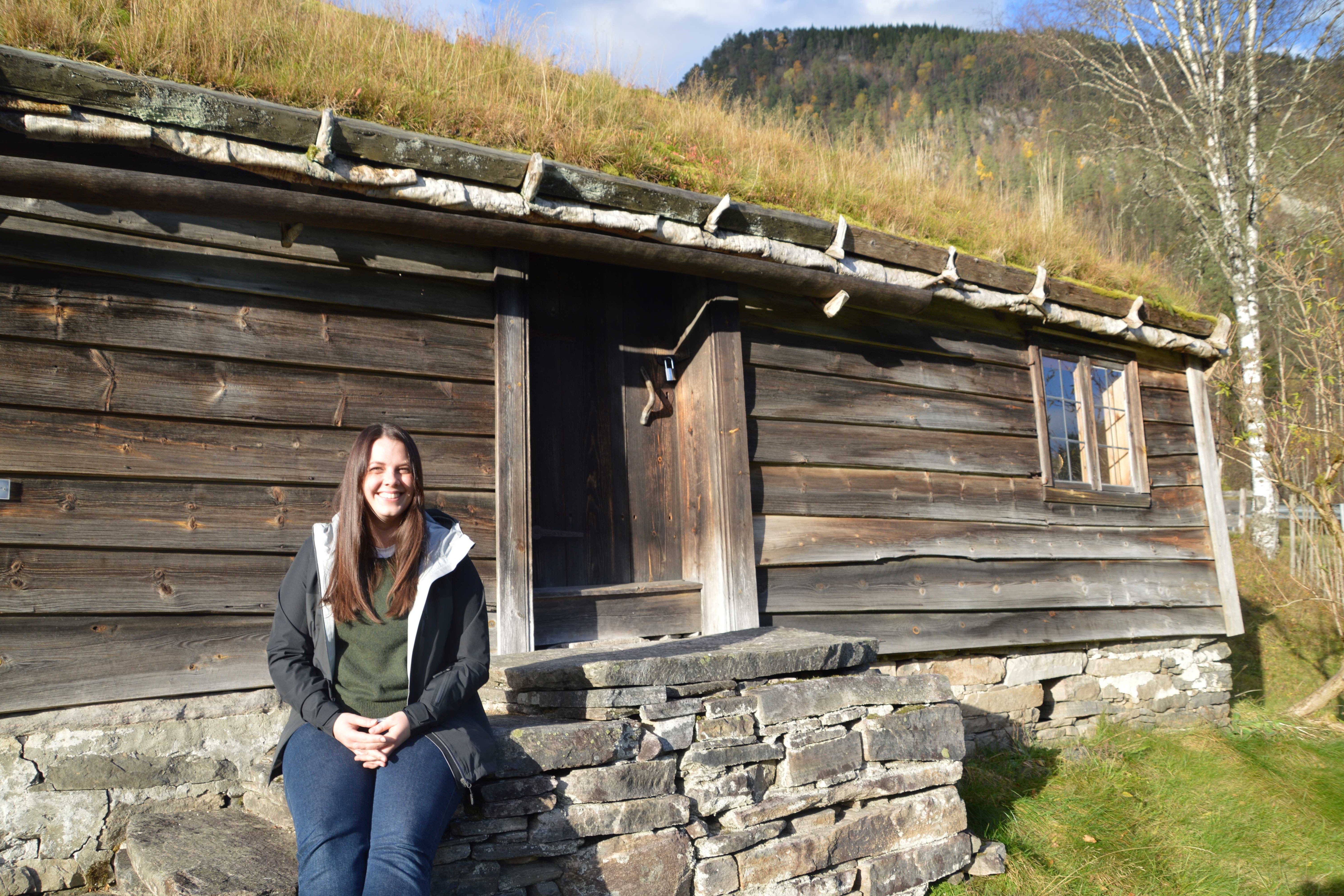 Konservatoren Kristine Ness sit foran huset på husmansplassen på Sunnfjord Museum.