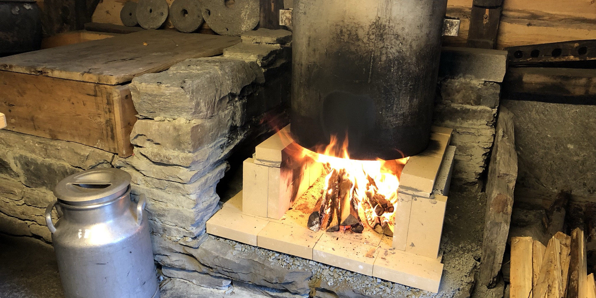 Ein stor kjele med lokk på står over ein open flamme i eit gamalt eldhus på Sunnfjord museum