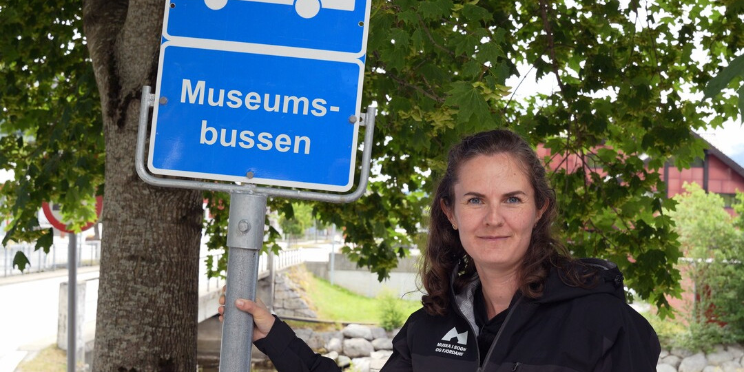 Dame står ved sidan av busskilt der det står Museumsbussen.