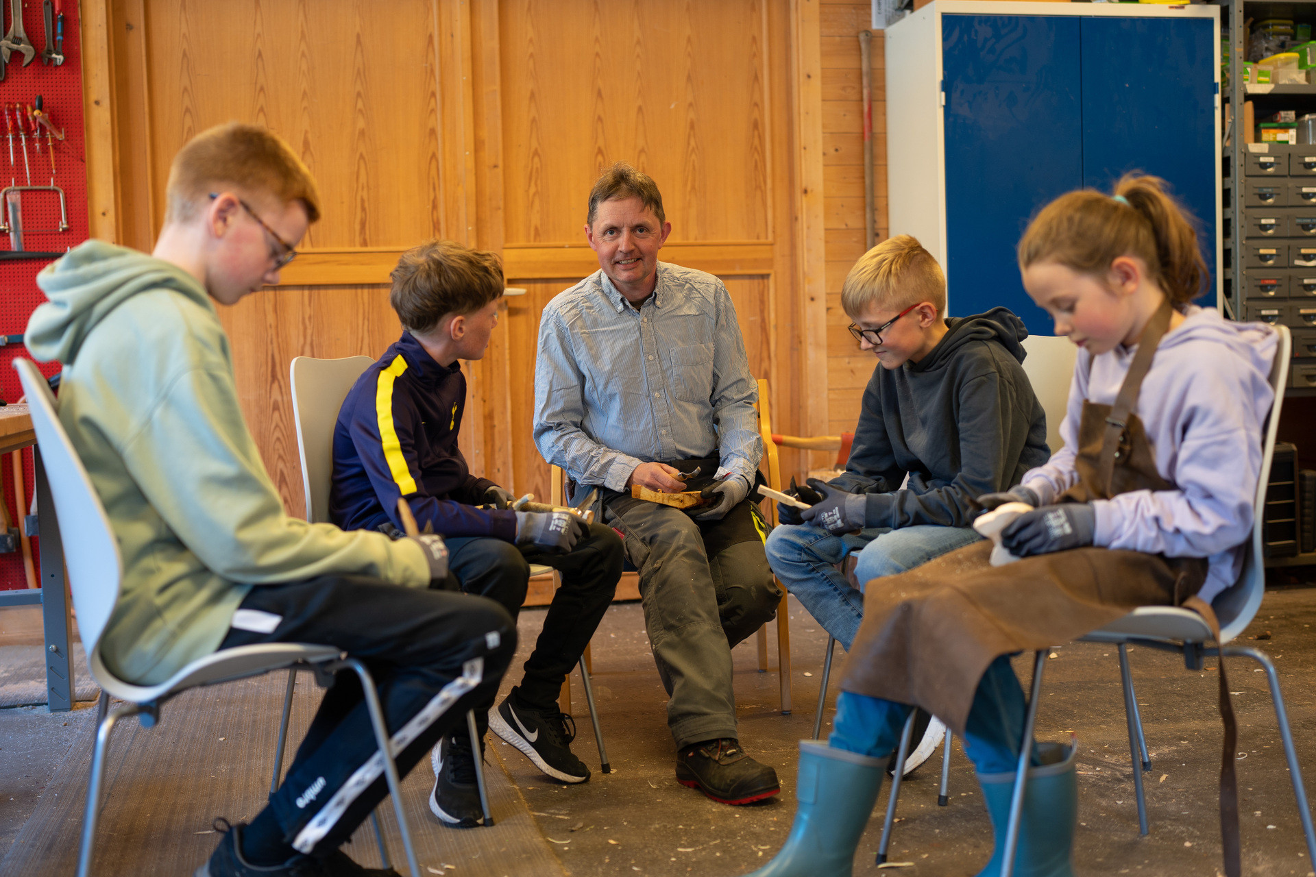 Ei gruppe barn sit og spikkar med kniv.