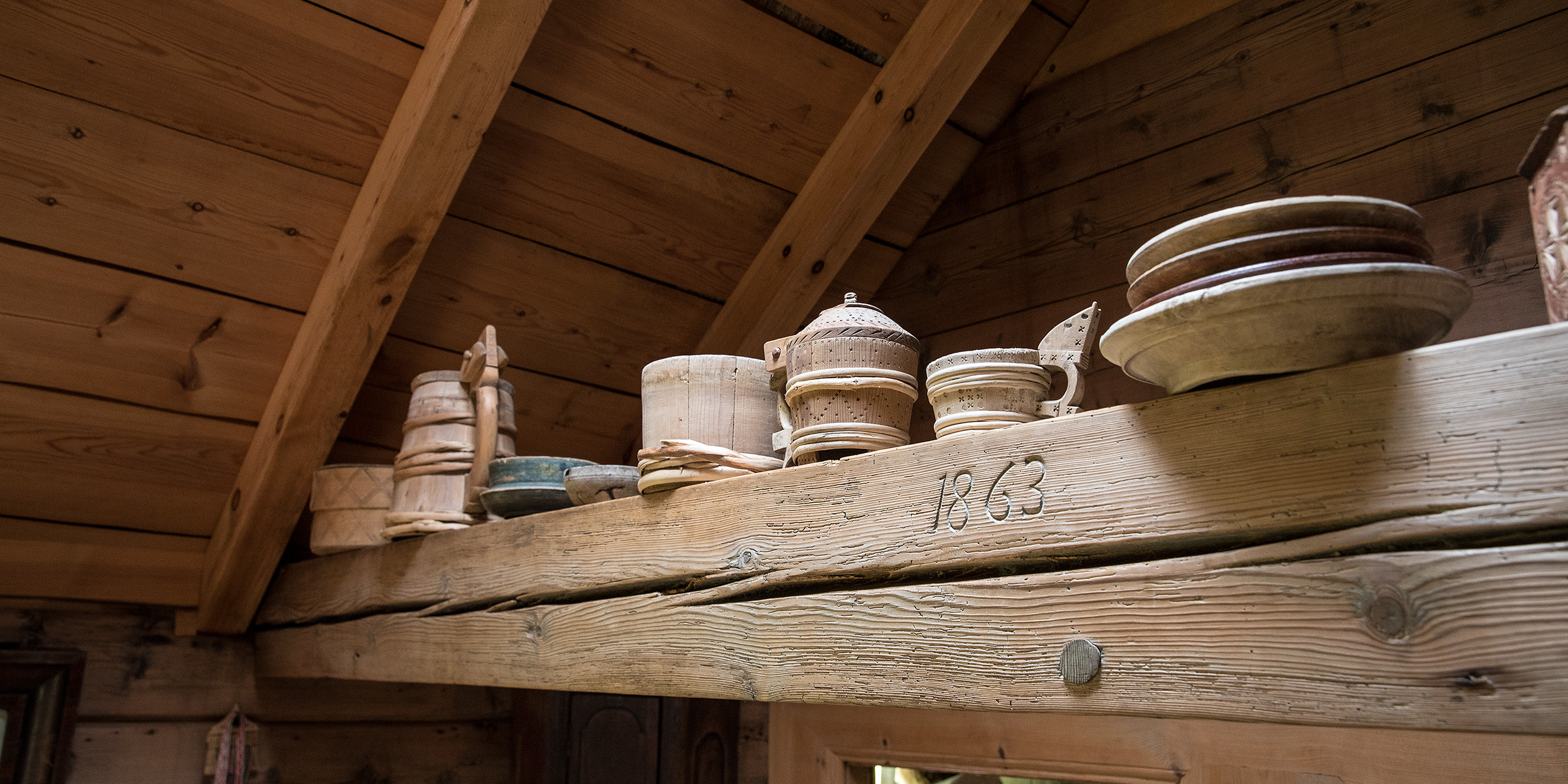 Innsida av ei stove. Mange tregjenstandar plassert oppå ein bete. Årstalet 1863 rissa inn i beten.