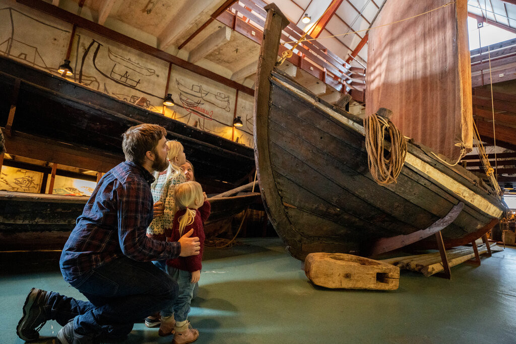 Familie med to barn ser påå på stor båt med segl inne i museum.